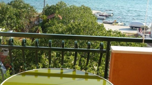 A balcony with a green table and striped chairs, overlooking a lake with boats and greenery. - in Poljica-Marina by Interhome (Trogir)