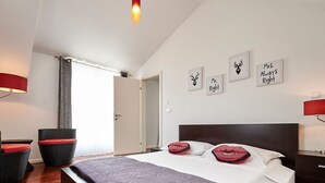 Ein modernes Hotelzimmer mit einem großen Bett, einem roten und schwarzen Sessel und einer Tür, die auf einen Balkon führt.