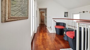 Ein Flur mit Holzboden, einer Treppe mit weißer Geländer und zwei Korbstühlen mit roten Kissen.