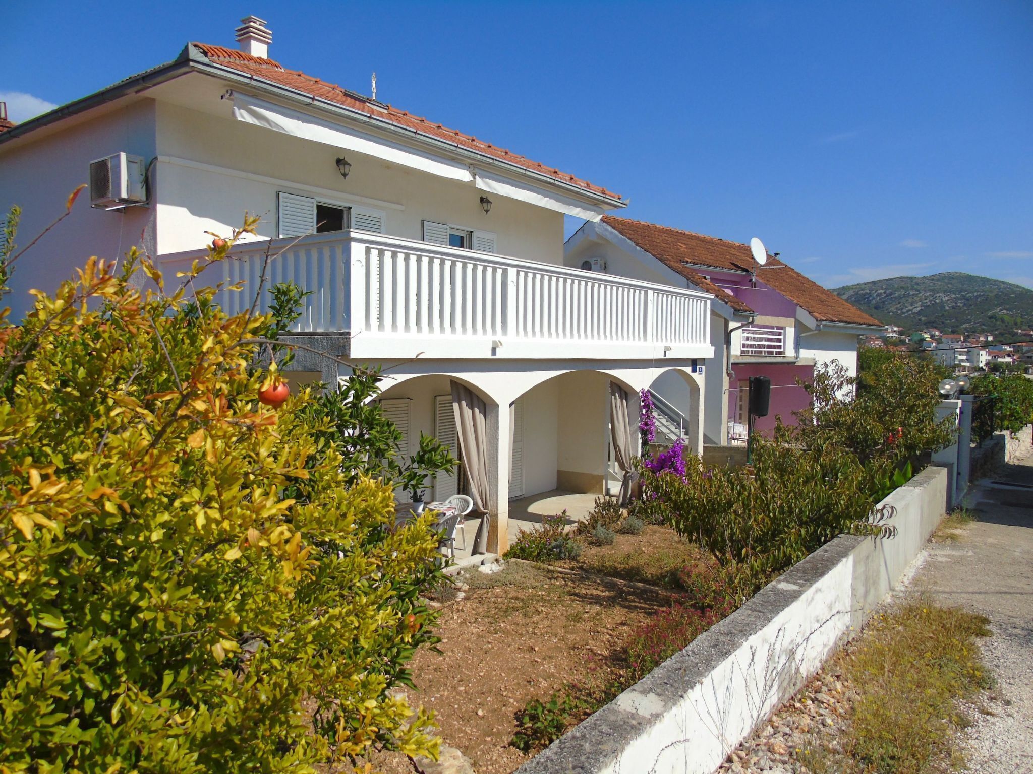 Ein zweistöckiges Gebäude mit Balkon, einem Garten mit Pflanzen und Blick auf die umliegende Nachbarschaft.