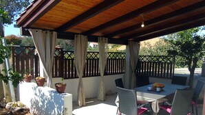 Une terrasse extérieure avec une table et des chaises, entourée de plantes en pot et d’une clôture en bois.