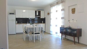 Une cuisine compacte avec des meubles blancs, une table à manger avec des chaises et une petite table d’appoint.
