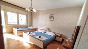 Ein Schlafzimmer mit zwei Betten, Holzboden, einer Kristallleuchter, einem kleinen Tisch und einem Fenster mit Vorhängen.