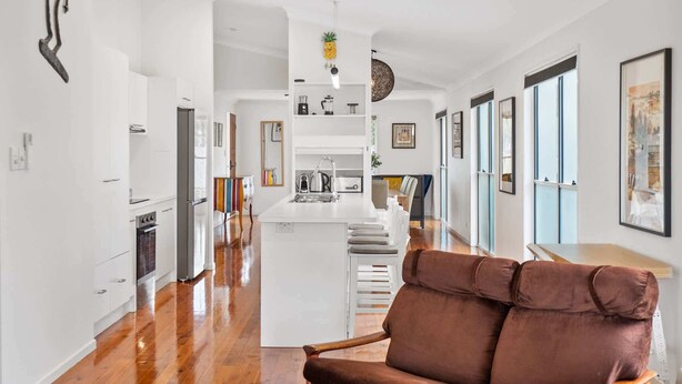 A modern kitchen with a central island, wooden flooring, and a brown leather chair in the foreground. - Bright 3-Bed Home in Leafy Annerley (Annerley)