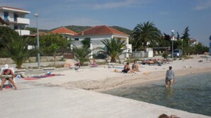 A beach with people sunbathing, a pool, and houses in the background.