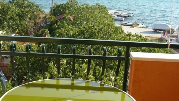 A balcony with a round table and striped chairs, overlooking a lake with boats and greenery.