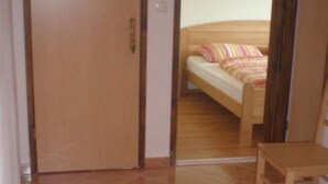 A room with a wooden door, a bed with striped bedding, and a wooden chair.