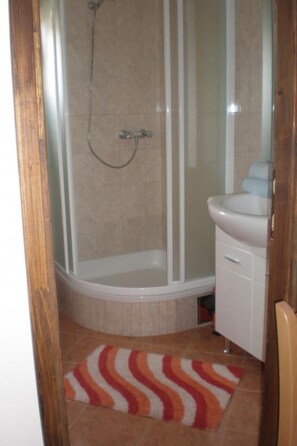 Ein Badezimmer mit einer gläsernen Duschkabine, einem weißen Waschbecken und einem Streifen-Teppich.