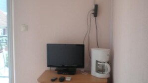 A corner room with a television on a wooden stand, a coffee maker, and an air conditioning unit mounted on the wall.