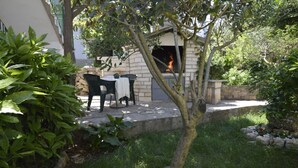Um pátio externo com lareira de pedra, cadeiras verdes e uma pequena mesa.