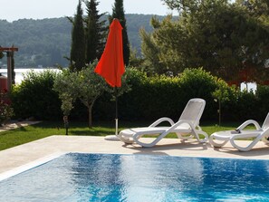 A swimming pool with two white lounge chairs and a red umbrella.