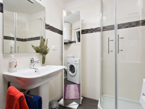A modern bathroom with a glass-enclosed shower, a sink with a mirror, a washing machine, and towels.