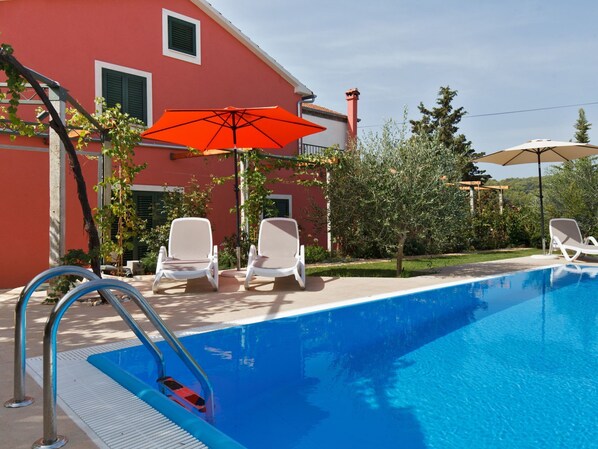 A swimming pool with two white lounge chairs and an orange umbrella.