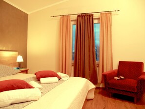 Une chambre d’hôtel comprenant un lit, deux oreillers, une chaise, une table de chevet avec une lampe et une fenêtre avec des rideaux.
