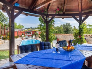 Un espace extérieur abrité avec une piscine, une table recouverte d’une nappe bleue et un panier de fruits.