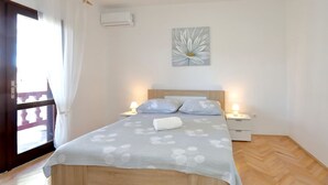 Ein Schlafzimmer mit einem hölzernen Bett, zwei Nachttischen mit Lampen, einer Wand-Klimaanlage und einem Fenster mit Vorhängen.