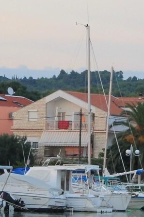 Un port de plaisance avec des bateaux amarrés, une maison dotée d’un balcon et, au loin, un paysage montagneux.
