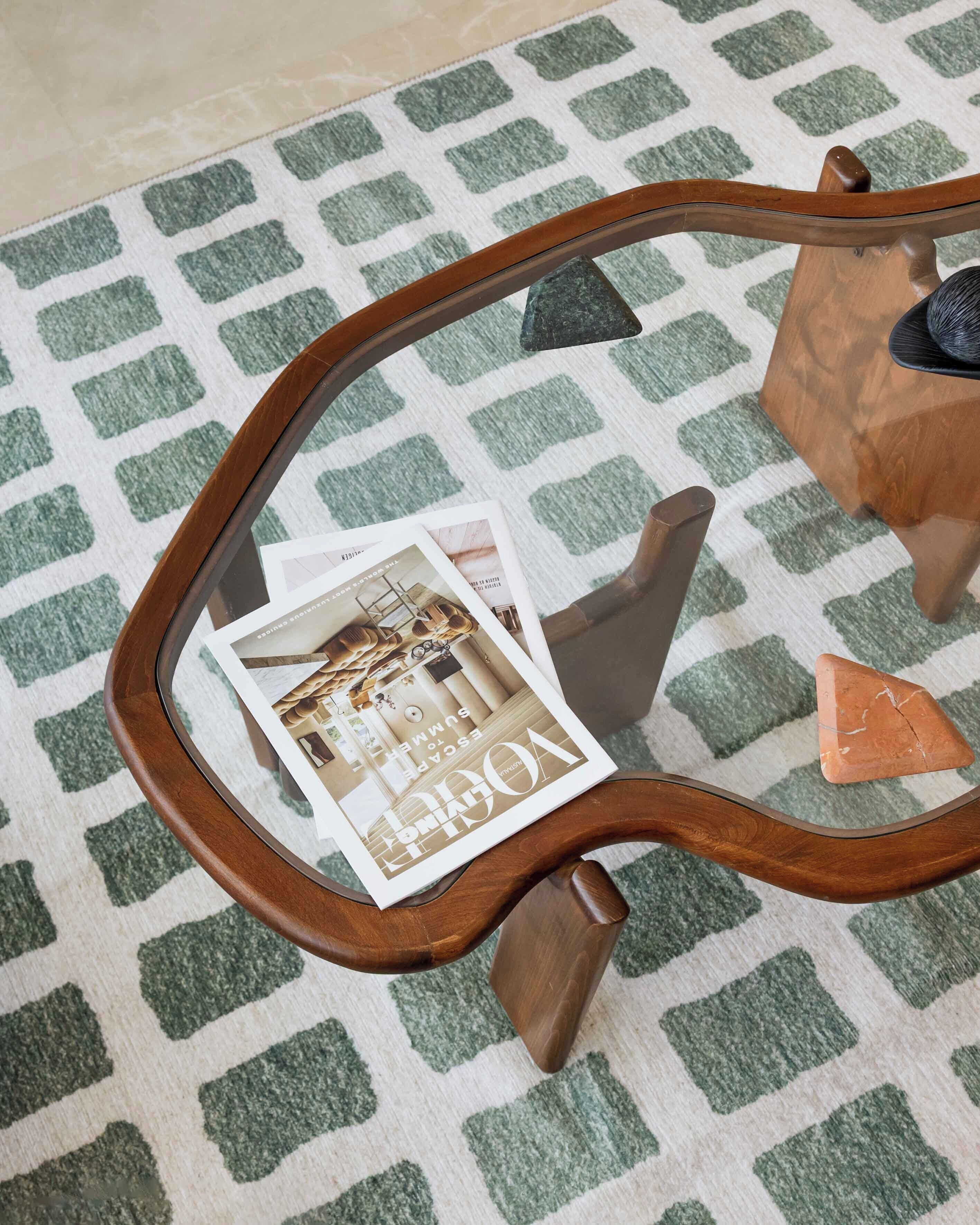 Una mesa de centro redonda de madera con tapa de cristal, con revistas y un pequeño objeto triangular.