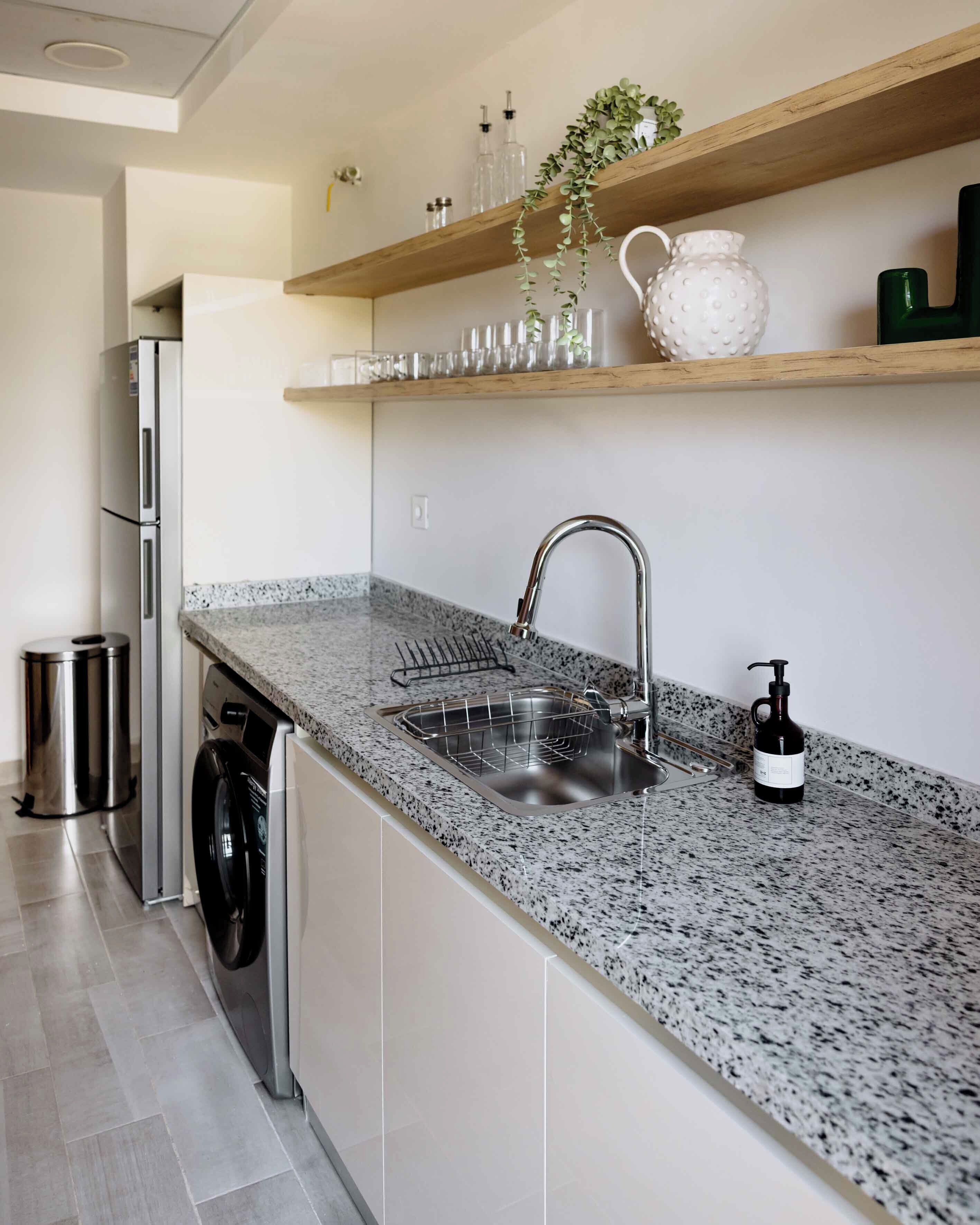 Una cocina con encimera de granito, electrodomésticos de acero inoxidable, un lavabo y una planta colgante.