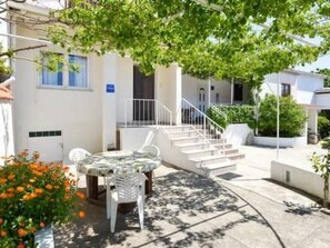 A white building with a staircase leading to a balcony. There is a table and chairs outside, and a potted plant with orange flowers. - Schönes Haus mit privatem Garten by Interhome (Zadar)