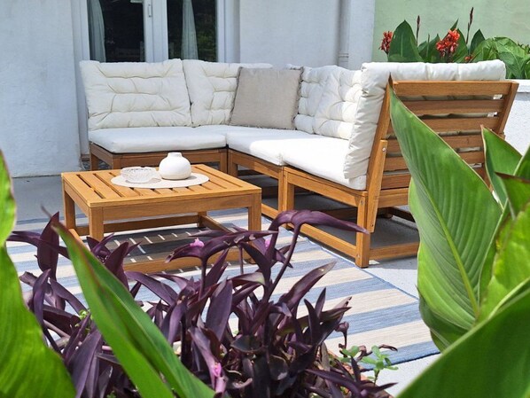 A cozy outdoor seating area with a cushioned sofa and wooden chairs, a small table with a vase and a teapot, surrounded by lush green plants. - Schönes Haus mit privatem Garten by Interhome (Zadar)