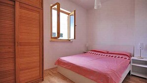 A bedroom with a wooden wardrobe, a bed with a pink bedspread, a bedside table, and a window. - mit Terrasse by Interhome (Zadar)