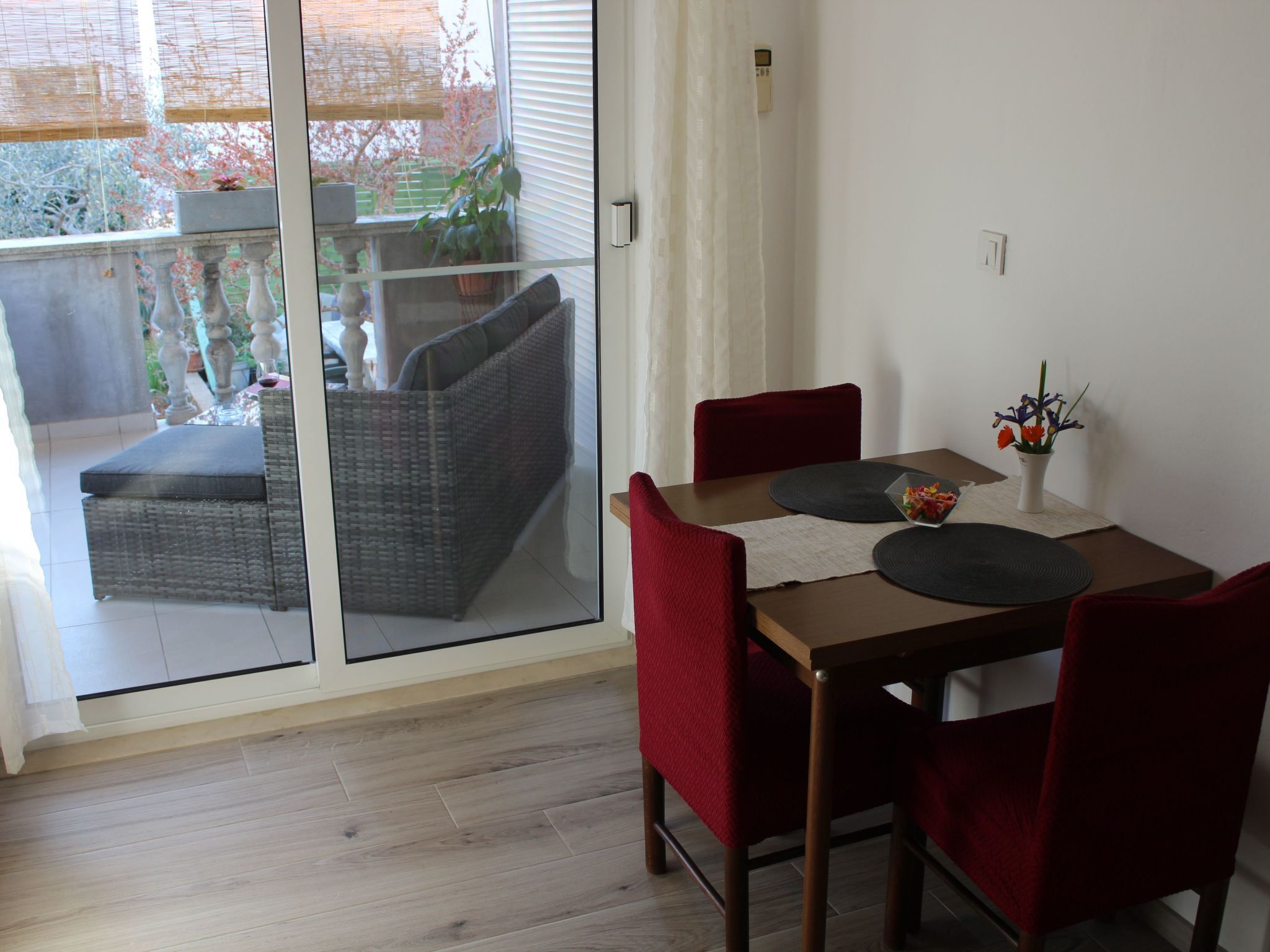 A dining area with a table, chairs, and a view through a glass door to an outdoor balcony with a sofa and plants.