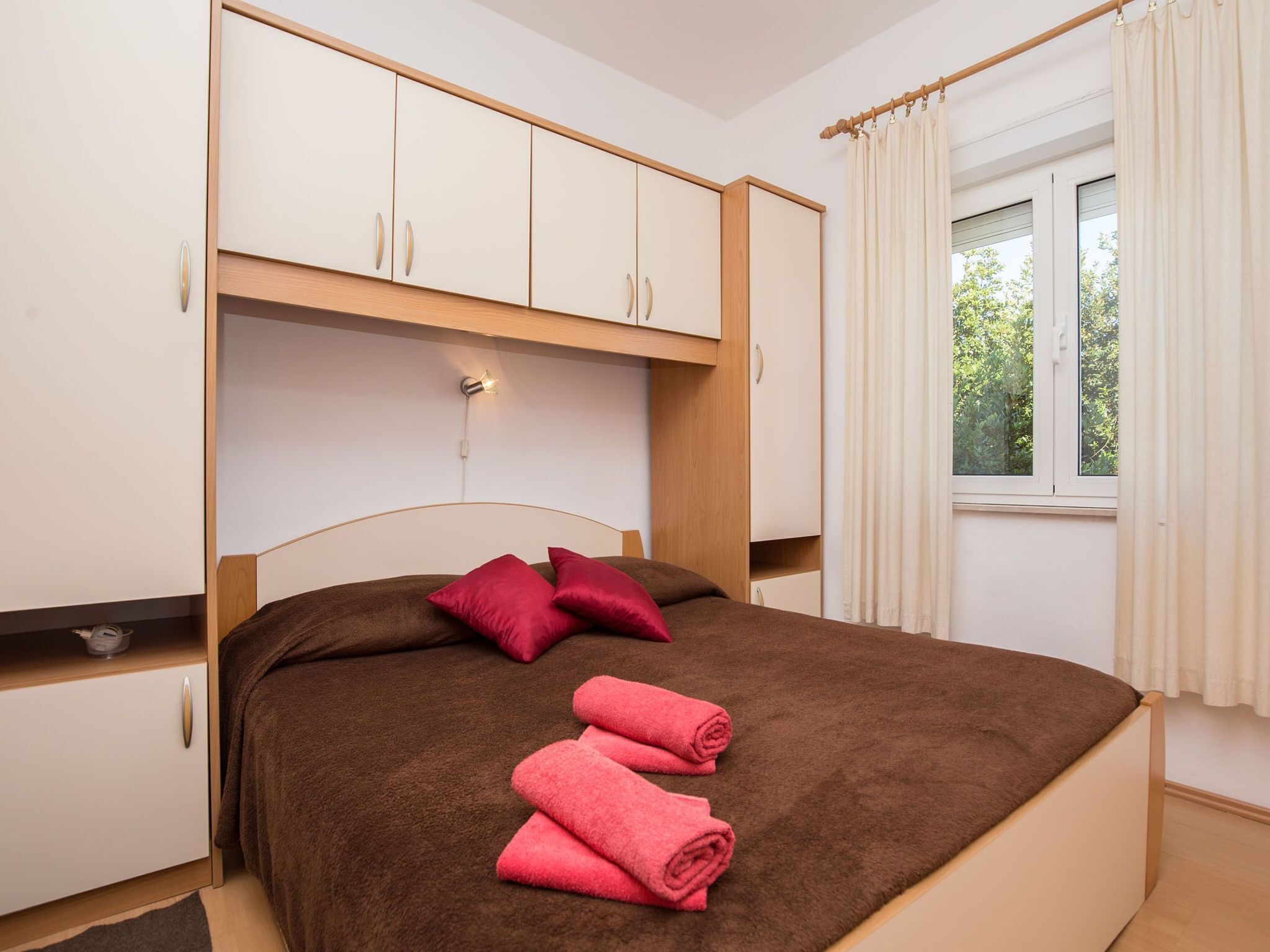 A bedroom with a bed, a wardrobe, a window with curtains, and a wall-mounted light.