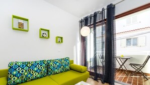 Ein helles Wohnzimmer mit einem grünen Sofa, einem weißen Couchtisch und Blick ins Freie durch leichte Vorhänge.