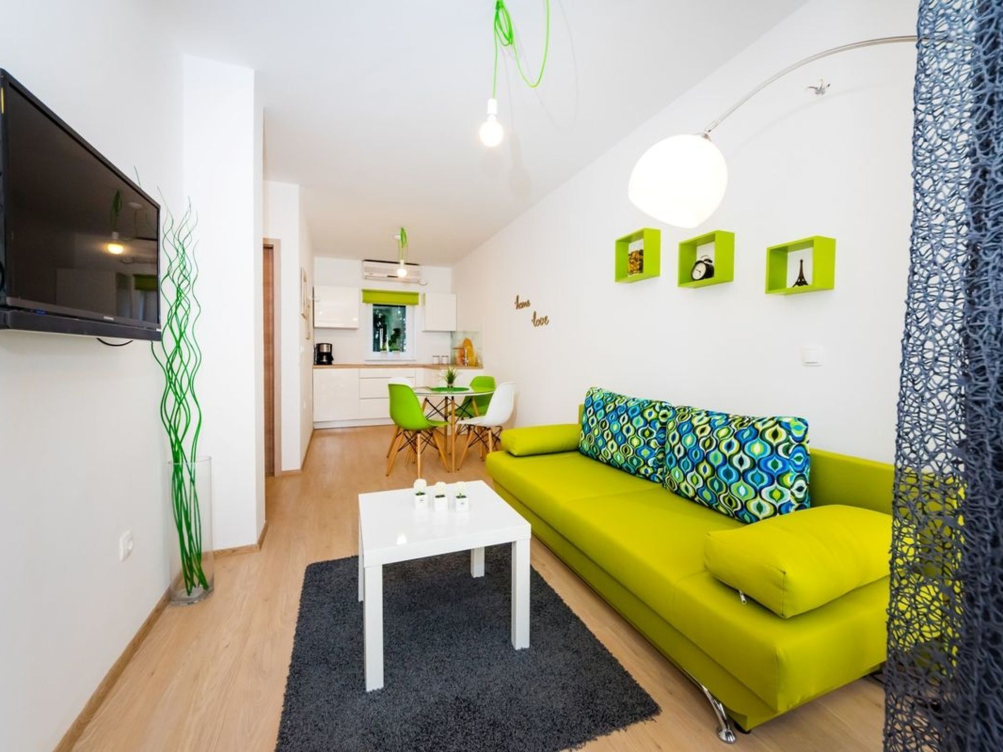 Un salon moderne avec un canapé vert vif, une table basse blanche et un téléviseur fixé au mur.