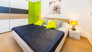 Ein modernes Schlafzimmer mit Bett, grünen Vorhängen, floraler Wandkunst und einer Nachttischlampe.