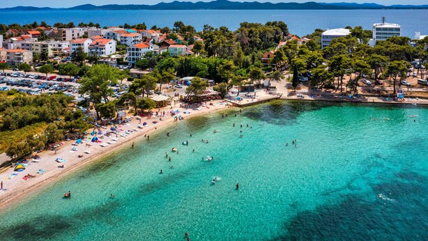 Une ville côtière dotée d’une plage, d’une eau turquoise cristalline et de bâtiments aux toits rouges.