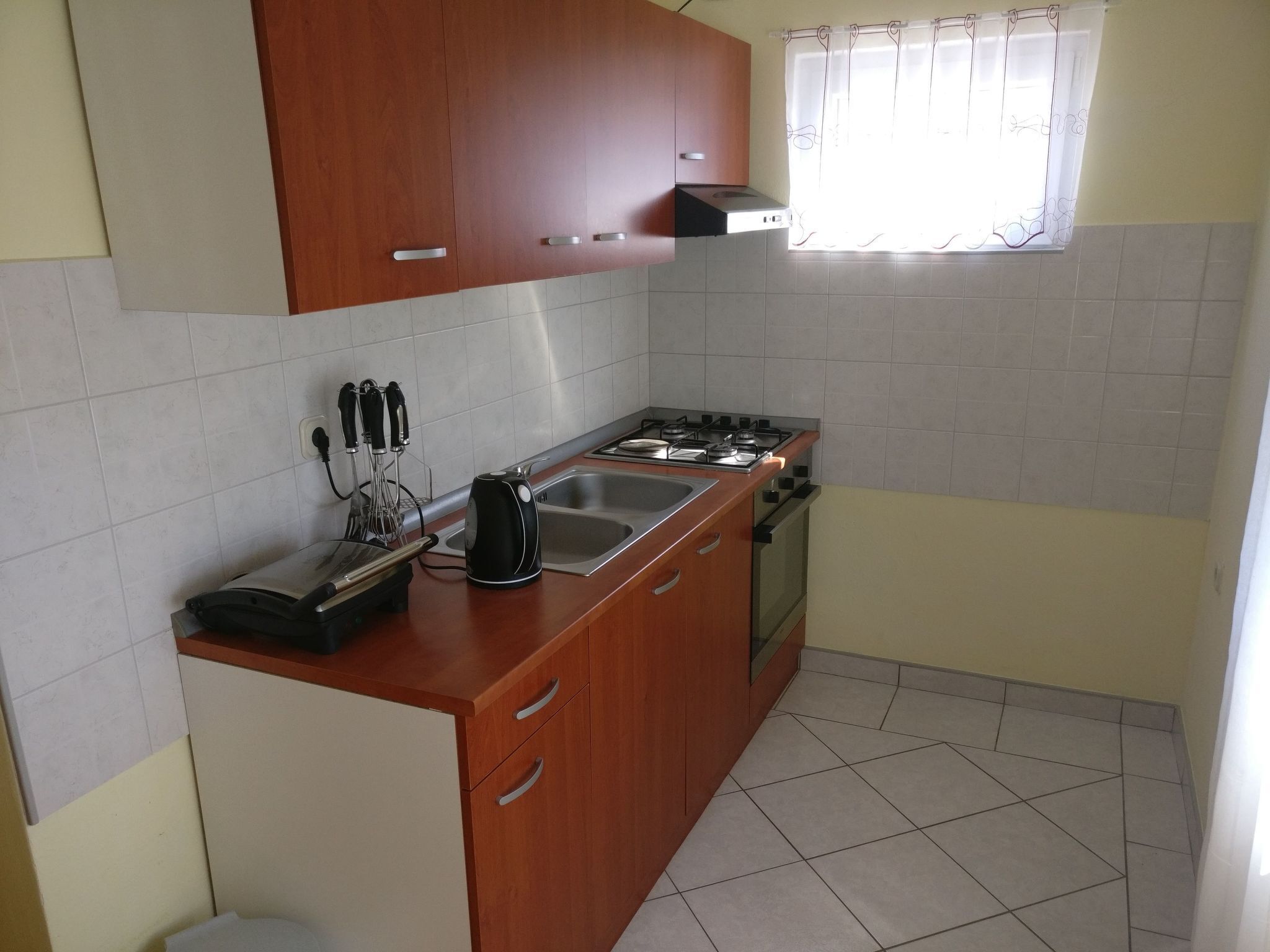 Une cuisine de taille réduite, dotée de meubles en bois, d’une cuisinière à gaz, d’un évier et d’une fenêtre avec un rideau.