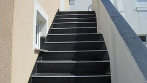 Una serie de escalones negros que conducen a un edificio con una pared exterior color crema y una ventana blanca.