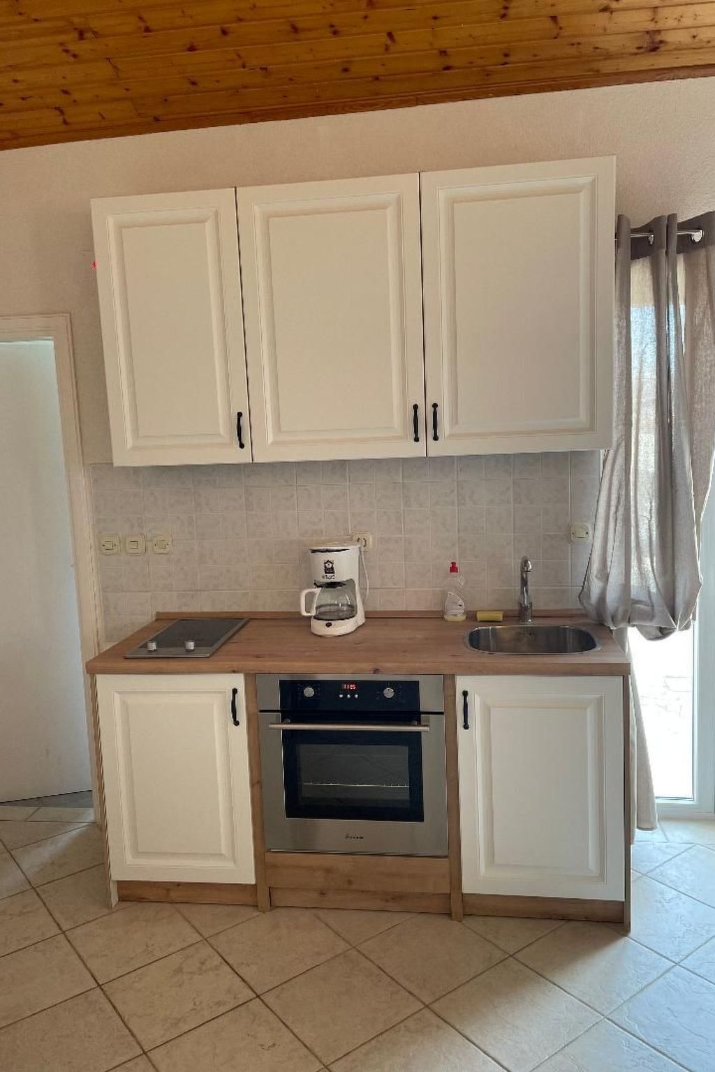 Cocina con gabinetes blancos, cafetera, lavabo y horno.