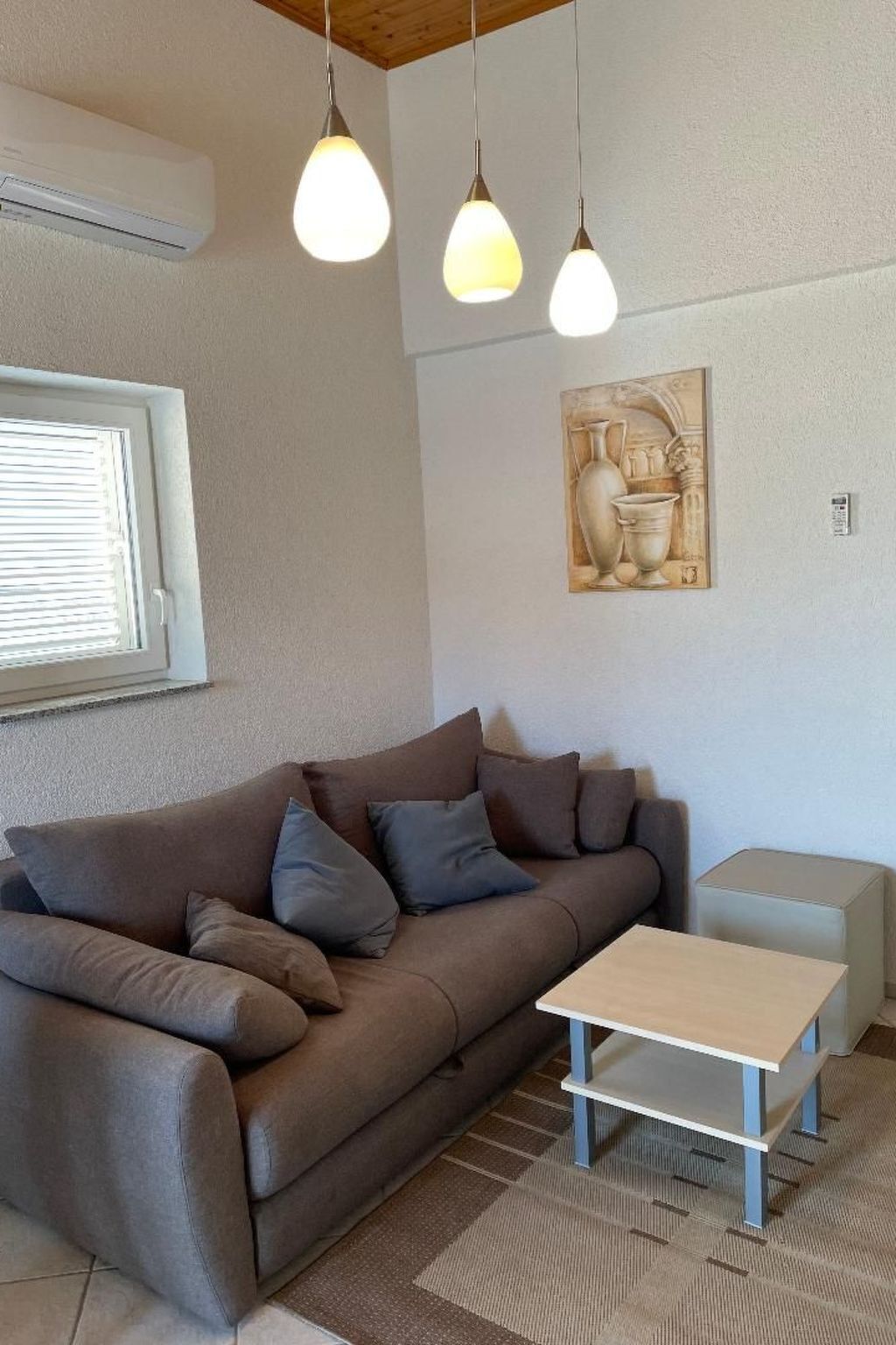 Een woonkamer met een bruine bank, een klein tafeltje en hanglampen.