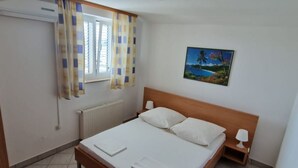 Un dormitorio con una cama grande, una ventana con cortinas, una mesita de noche, una lámpara de pared y un cuadro.