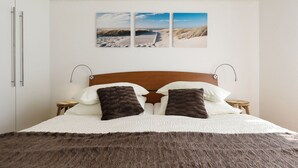 A bed with a wooden headboard, two white pillows, two dark brown pillows, and a brown furry blanket. There are two bedside tables with lamps. - mit Blick auf das Wasser by Interhome (Vir)
