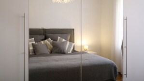 Un dormitorio con cama, almohadas, una mesita de noche y una lámpara colgante.