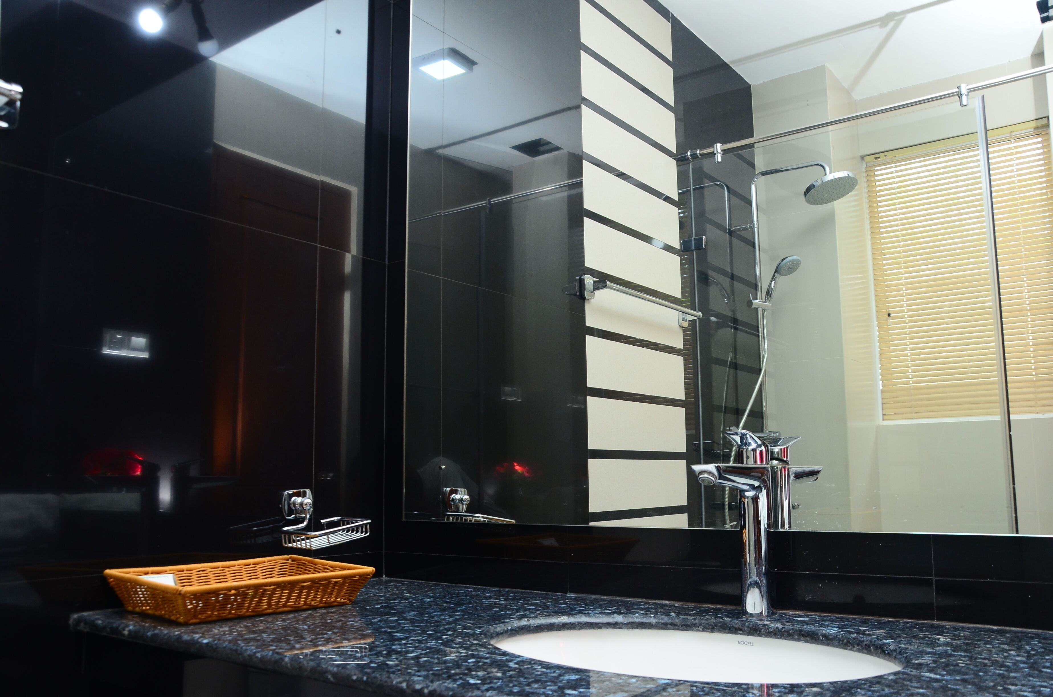 A modern bathroom with a black tiled wall, a large mirror, a chrome sink, and a shower with a glass enclosure.