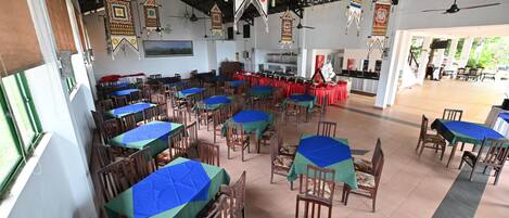 A spacious dining area with tables covered in blue and green tablecloths, wooden chairs, and hanging decorative elements.