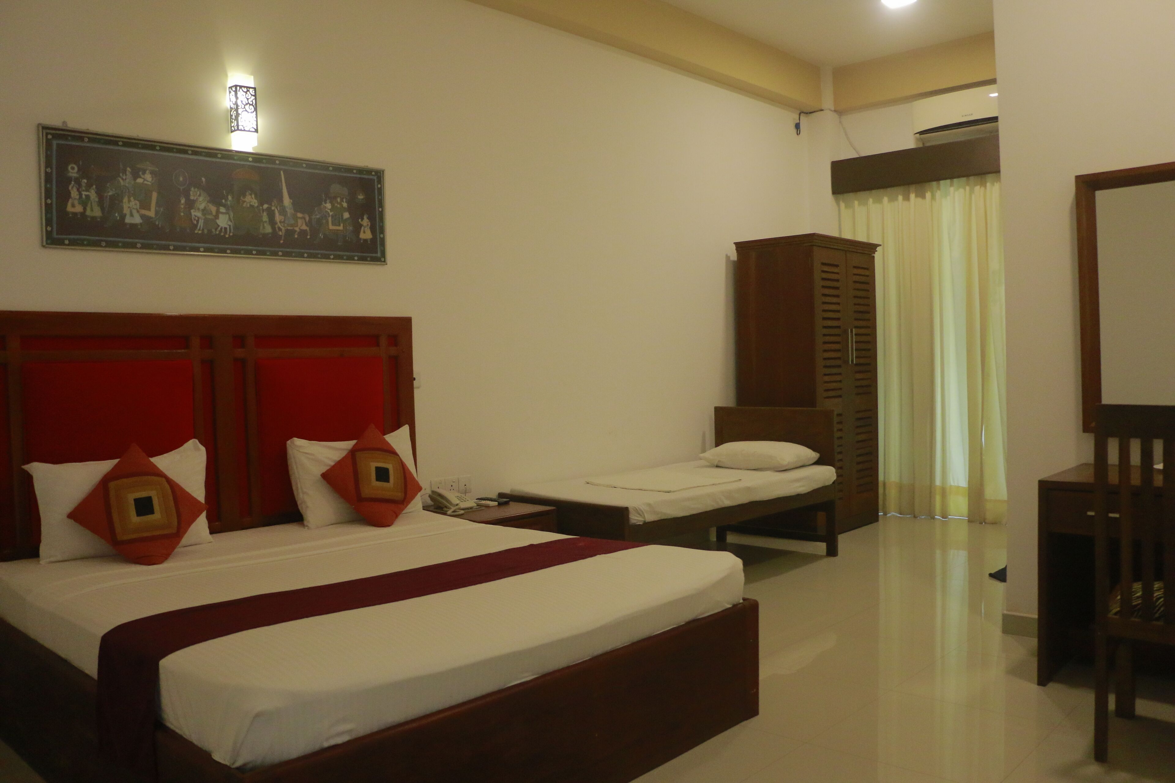 A hotel room with a large bed, a smaller bed, a wardrobe, a desk, and a chair.