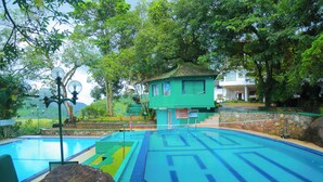 A pool area with a small building, surrounded by trees and a clear sky. - Wijaya Holiday Resort (Kiriella)