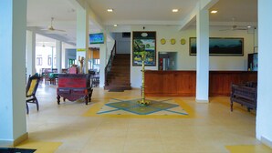 A spacious lobby with a reception desk, a staircase, and a large painting on the wall. - Wijaya Holiday Resort (Kiriella)