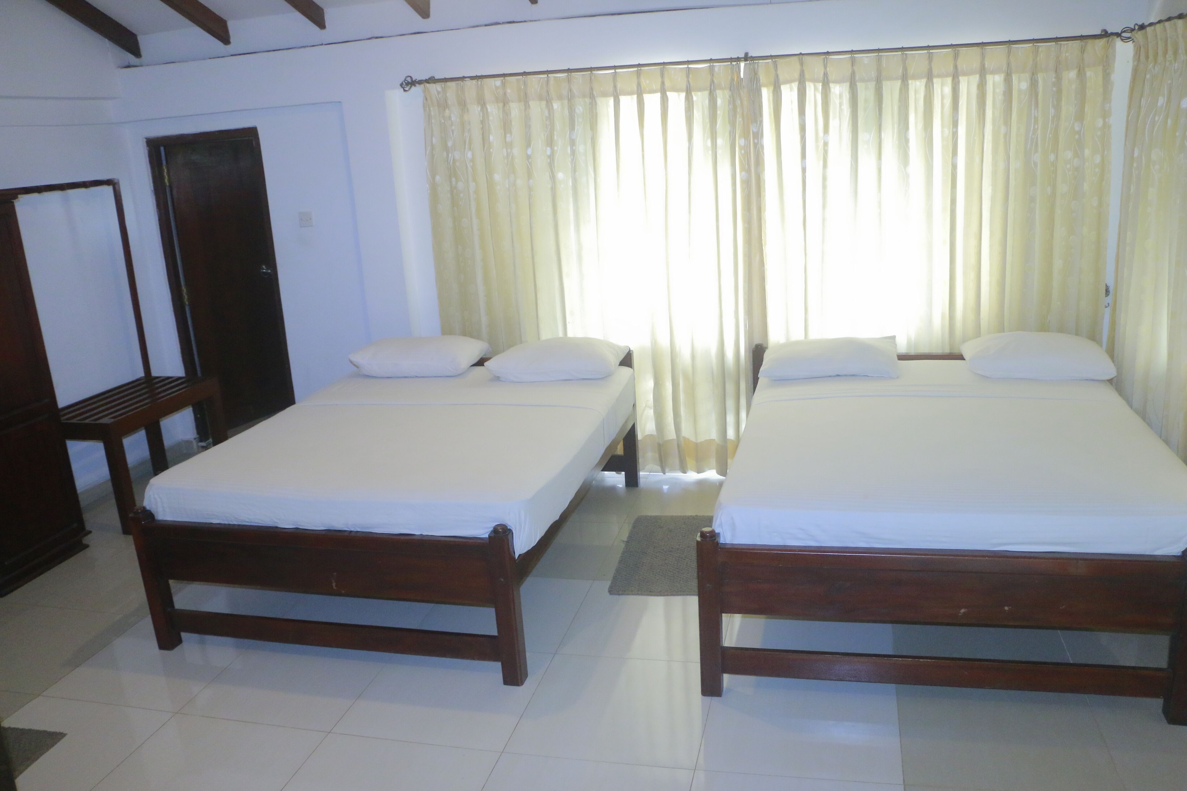 Habitación de hotel con dos camas de madera, un armario de madera y un ventanal con cortinas.