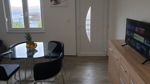 A modern living room with a glass dining table, black chairs, a TV on a wooden stand, and a view of the sea through a door. - Wohnung in Cesarica mit Privater Terrasse by Interhome (Karlobag)