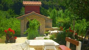 Un área de comedor al aire libre con una mesa y sillas de piedra, rodeada de follaje y una pequeña construcción de ladrillo.