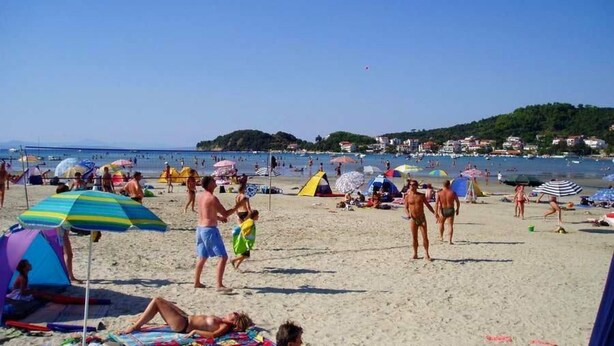 Una playa con gente tomando el sol y nadando, tiendas de campaña y sombrillas.