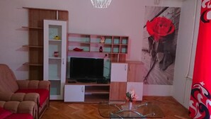 Una sala de estar con un sofá, una mesa de centro de vidrio, un televisor, un mueble de madera y una cortina roja.