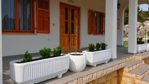A building with a number '109B' above the entrance, wooden shutters on windows, and white planters with plants on the porch. - Fantastisches Haus nur 700m vom Strand entfernt by Interhome (Rab/Kampor)